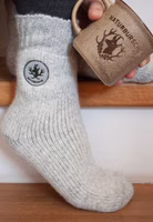jemand sitzend auf Treppenstufen mit einem Paar hellgrau melierten Naturbursche Stricksocken mit Hirsch-Patch und dem Schriftzug Naturbursche im oberen Bereich