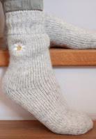 jemand sitzend auf Treppenstufen mit einem Paar hellgrau melierten Glücksbringer Stricksocken mit hübscher Edelweißblüten-Stickerei im oberen Bereich