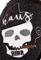 Nahaufnahme einer weißer Totenkopfstickerei, brauner Zigarre im Mund und Hausherr-Schriftzug auf schwarzem Filz