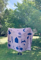 im Garten hochgehalten eine rosa und dunkelblaue Kuscheldecke mit abstrakten Motiven von Blumen, Fahrrad, Katze, Mond 