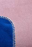 Nahaufnahme der weiß eingefassten Webkante einer rosa und dunkelblauen Kuscheldecke mit abstrakten Motiven von Blumen, Fahrrad, Katze, Mond