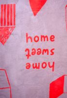Nahaufnahme einer beige- und korallefarbenen Kuscheldecke mit abstrakten Häusern sowie Schriftzug Home sweet Home 