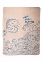 eine beige Kuscheldecke mit dem blaugrauen Motiv einer Scholle und den schwungvollen Konturen von Meereswellen sowie dem Schriftzug Mein lieber Scholli 