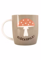 eine taupe-grün farbende Henkeltasse aus Porzellan mit dem dunkelbraunen Schriftzug Glückspilz und darüber ein Fliegenpilz mit pastellorangem Hut