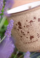 hellbrauner Henkelbecher aus Porzellan mit dunkelbraunem Gardenlover Motiv von Anna Katharina Jansen vorne und in dem Becher ein kleines Kleeblatt