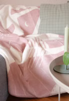 eine creme- und rosafarbene Kuscheldecke mit abstrakten Figuren der Illustratorin Halfbird liegend auf einem Sofa im Wohnzimmer