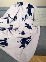 eine helllila-farbene Kuscheldecke mit dem dunkelblauen Motiv von verschiedenen Hundebesitzern mit deren Hunden zum Teil an der Leine liegend auf einem Sofa