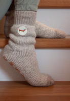 jemand sitzend auf Treppenstufen mit einem Paar beige melierten Gut (v)erzogen Stricksocken mit Dackel-Patch im oberen Bereich und dunkler beige abgesetzten Bündchen und Zehenteil