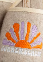 auf sandfarbenem Filz aufgesticktes Motiv einer aufgehenden Sonne in orange und lila sowie darunter mit dem Schriftzug Sonnenschein in weiß