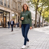A woman wearing a green leather jacket and jeans is walking down a cobblestone shopping street with a coffee mug