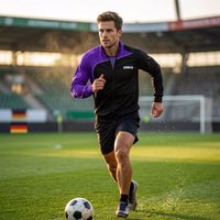 A man plays football on an outdoor court, wearing an OMKA training jacekt. A football hoop is visible in the background.