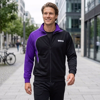 A man is walking down the street, wearing an OMKA tracksuit jacket with a stand-up collar. A subway sign is visible in the background.