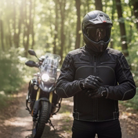A motorcyclist wearing a black textile jacket puts on protective gloves in front of a travel enduro bike on a sunny forest path