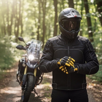 Motorradfahrer in schwarzer Textiljacke zieht Schutzhandschuhe an vor einer Reiseenduro auf einem sonnigen Waldweg