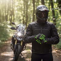 A motorcyclist wearing a black textile jacket puts on protective gloves in front of a travel enduro bike on a sunny forest path