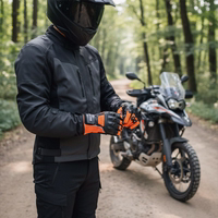 Motorradfahrer in schwarzer Textiljacke zieht Schutzhandschuhe an vor einer Reiseenduro auf einem sonnigen Waldweg