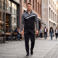 Model standing on city wearing STRIKER gray/black track suit with "German Wear" text. White stripe on chest and pants.