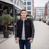Herren in schwarz Collegejacke mit schwarzen Lederärmeln und Jeans geht über einen gepflasterten Gehweg in der Stadt