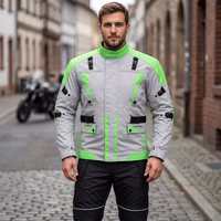 Cordura-Textil-Motorradjacken Herren steht auf der Straße, trägt Motorradjacke mit Protektoren. Motorräder im Hintergrund sichtbar.