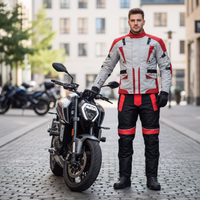 Cordura-Textil-Motorradjacken Herren steht auf der Straße, trägt Motorradjacke mit Protektoren. Motorräder im Hintergrund sichtbar.