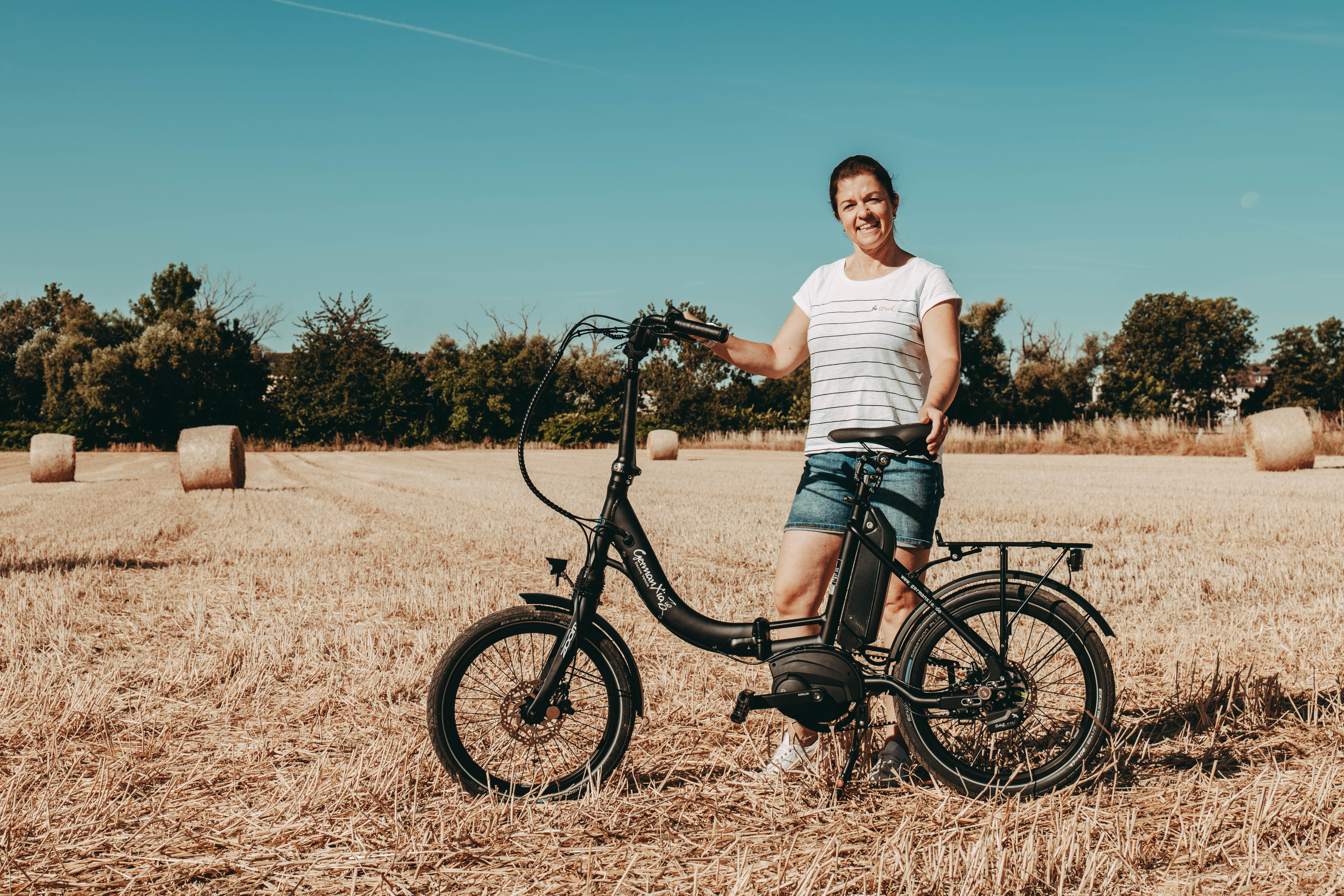 Hotelbesitzerin nutzt das schwarze GermanXia Mobilemaster E-14 PP Klapp-E-Bike für Ausflüge in der Natur