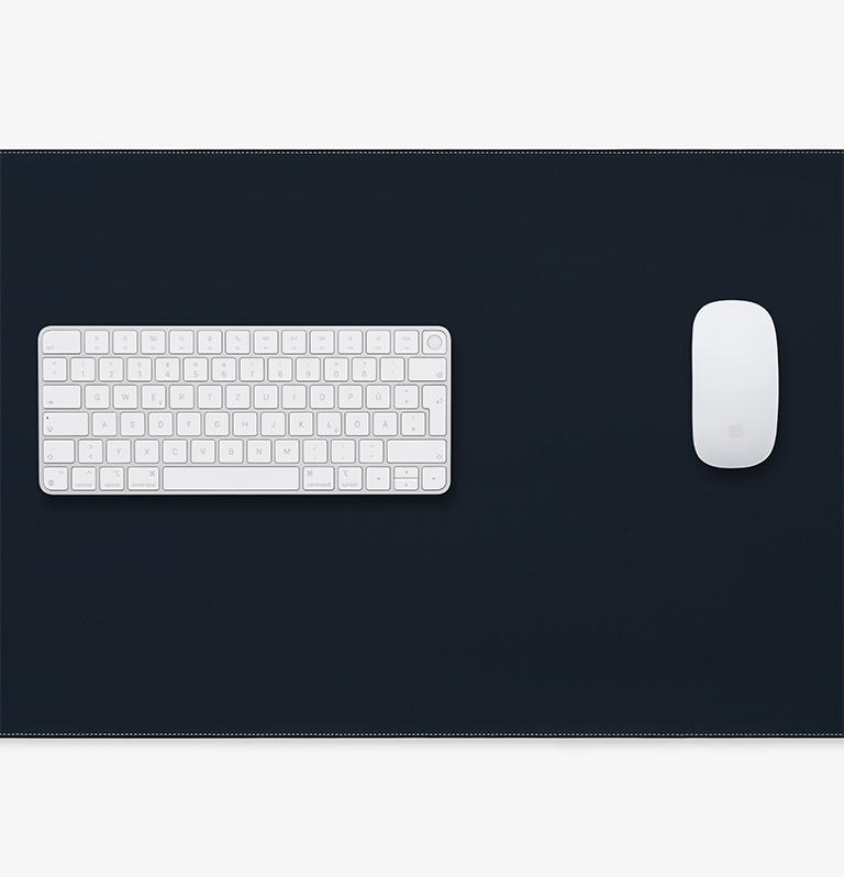 Schreibtischmatte aus pflanzlich gegerbtem schwarzem Leder mit Apple Tastatur und Apple Maus, umlaufender weißer Sichtnaht und Logoprägung, Draufsicht